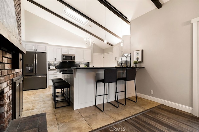 kitchen with a kitchen bar, tasteful backsplash, appliances with stainless steel finishes, kitchen peninsula, and white cabinets