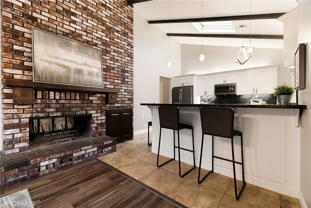 kitchen featuring beamed ceiling, white cabinetry, kitchen peninsula, stainless steel appliances, and a brick fireplace