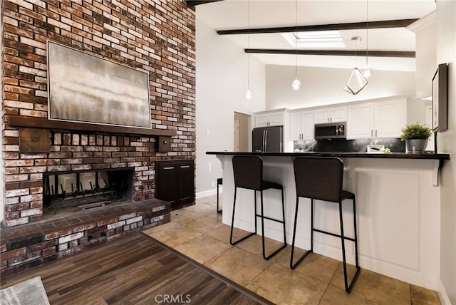 kitchen with a brick fireplace, kitchen peninsula, beamed ceiling, stainless steel appliances, and white cabinets