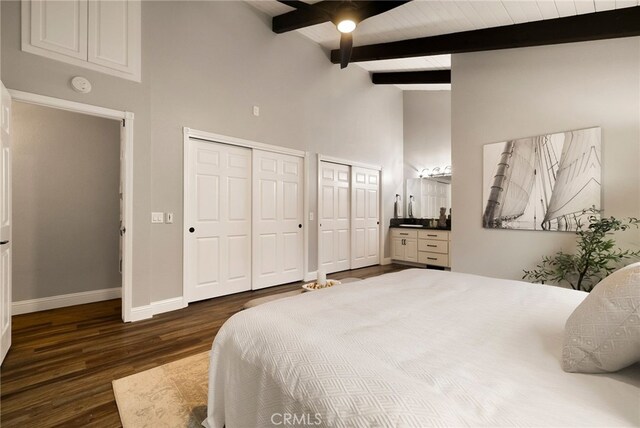 bedroom with dark hardwood / wood-style floors, two closets, high vaulted ceiling, beamed ceiling, and ceiling fan