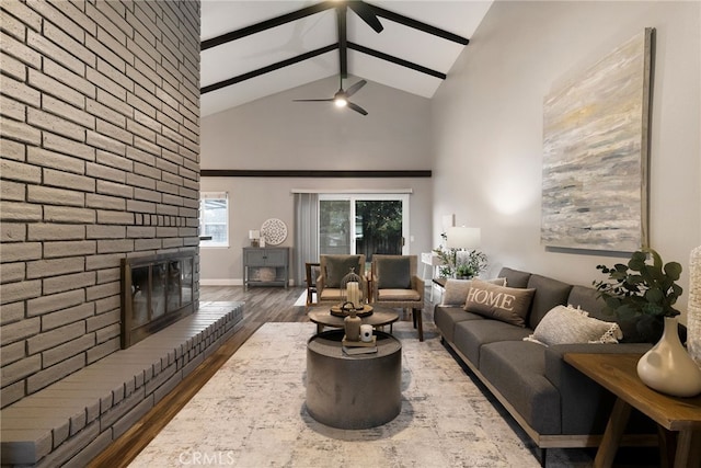 living room featuring high vaulted ceiling, wood-type flooring, ceiling fan, a brick fireplace, and beam ceiling