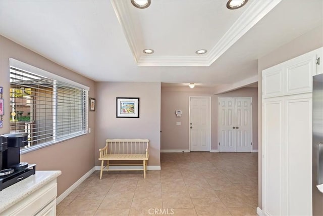 corridor featuring a raised ceiling, light tile patterned flooring, and crown molding