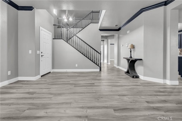 entryway with light hardwood / wood-style floors, crown molding, and a chandelier