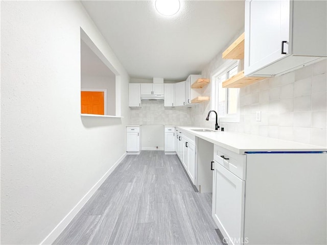 kitchen with tasteful backsplash, white cabinets, light wood-type flooring, and sink