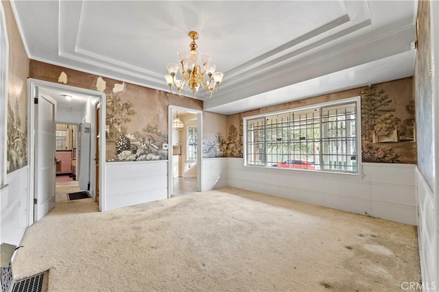 carpeted spare room featuring an inviting chandelier and a raised ceiling