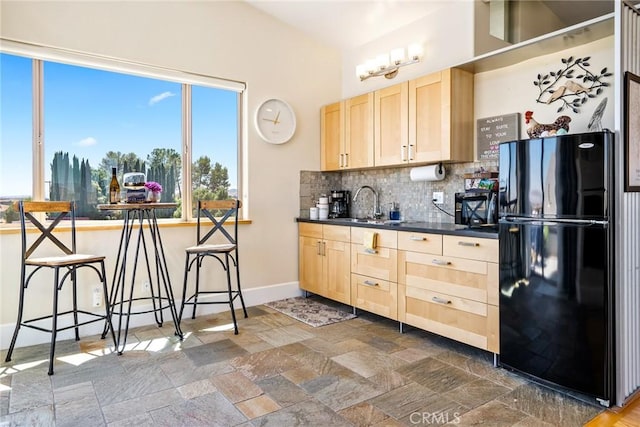 kitchen featuring stone tile flooring, decorative backsplash, black appliances, light brown cabinetry, and dark countertops