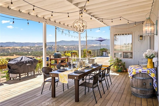 deck with outdoor dining space, a mountain view, and a grill