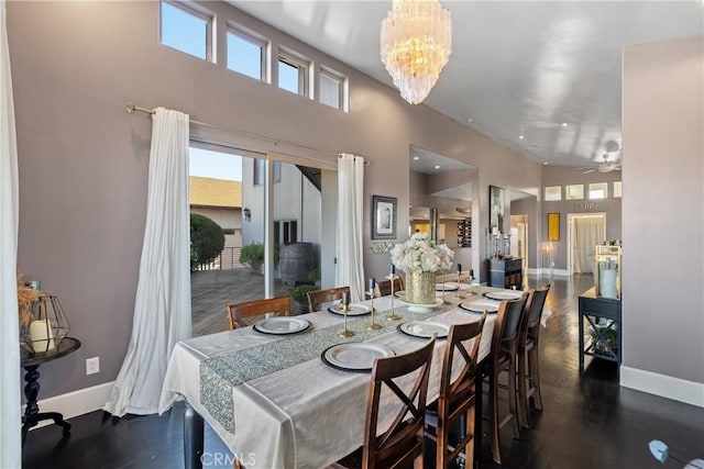 dining space featuring wood finished floors, a high ceiling, ceiling fan with notable chandelier, and baseboards