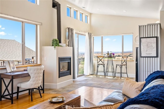 living room with a glass covered fireplace, high vaulted ceiling, baseboards, and wood finished floors