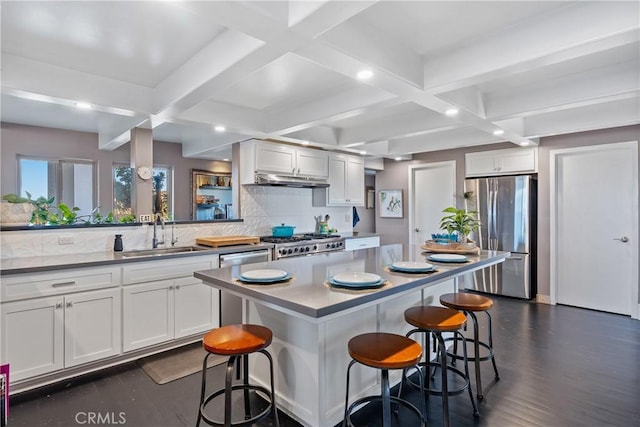 kitchen featuring a breakfast bar, freestanding refrigerator, stove, white cabinets, and a sink