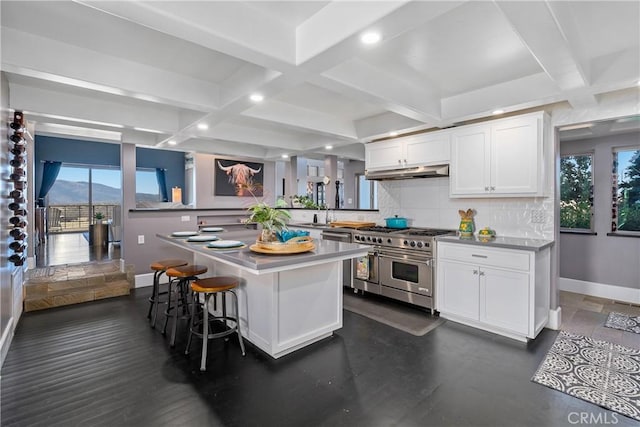 kitchen with a kitchen bar, coffered ceiling, a center island, range with two ovens, and white cabinets