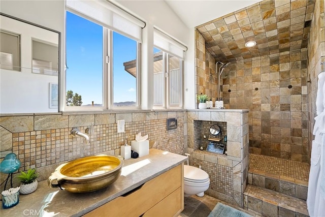 bathroom featuring toilet, tile walls, vanity, and a tile shower