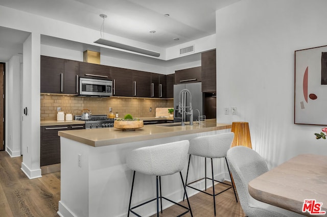 kitchen featuring appliances with stainless steel finishes, tasteful backsplash, kitchen peninsula, hardwood / wood-style flooring, and a breakfast bar