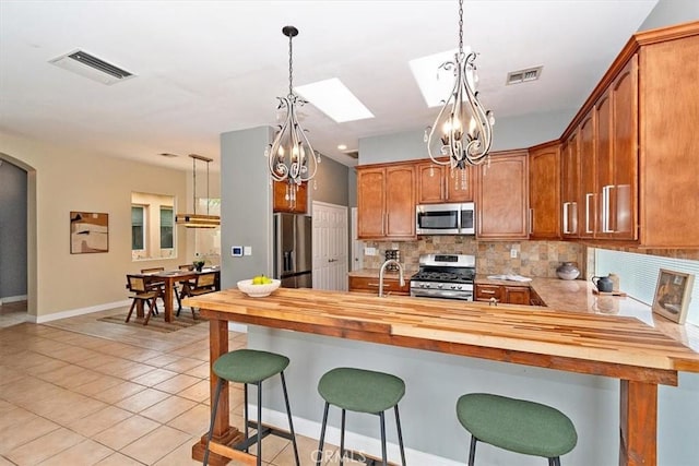 kitchen featuring a skylight, butcher block counters, appliances with stainless steel finishes, tasteful backsplash, and light tile patterned flooring