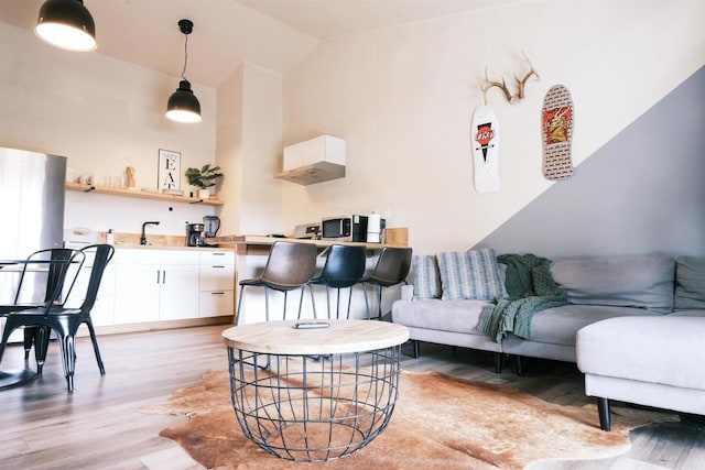 living room featuring light wood-type flooring, vaulted ceiling, and sink