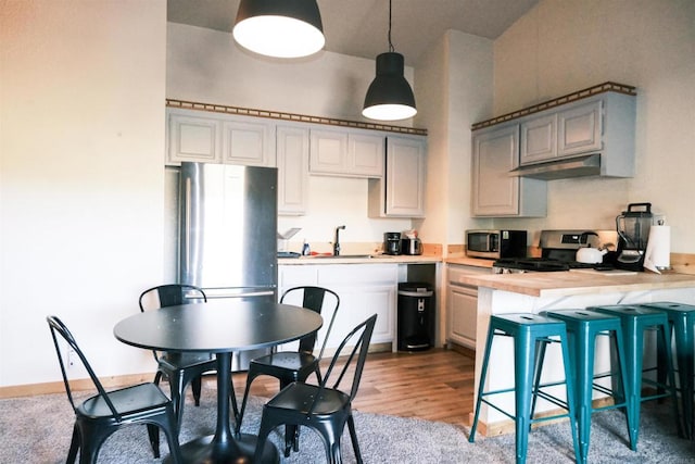 kitchen featuring wood counters, decorative light fixtures, stainless steel appliances, sink, and a breakfast bar area