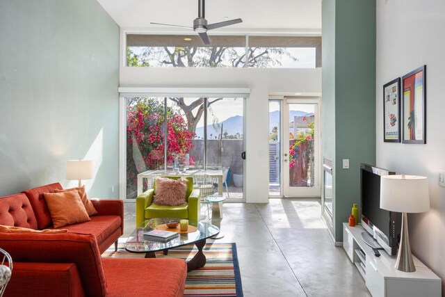 living room with ceiling fan, a high ceiling, and concrete flooring