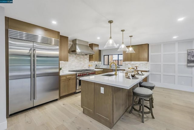 kitchen with sink, high end appliances, tasteful backsplash, hanging light fixtures, and wall chimney range hood