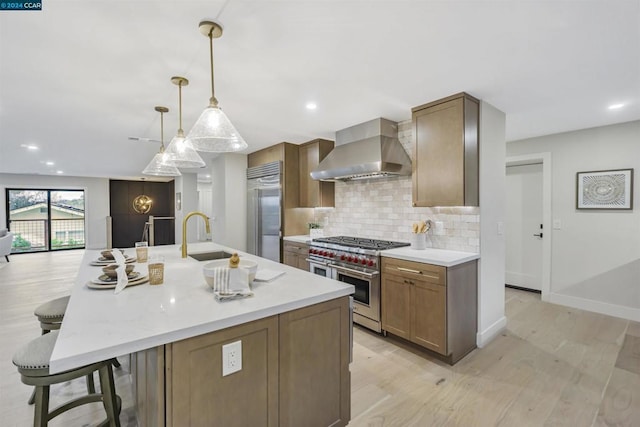 kitchen with hanging light fixtures, a center island with sink, high quality appliances, a kitchen breakfast bar, and wall chimney range hood