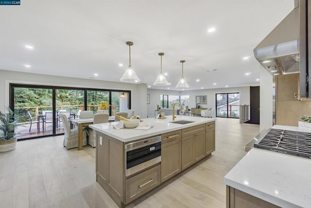 kitchen featuring sink, hanging light fixtures, range hood, a center island with sink, and light wood-type flooring