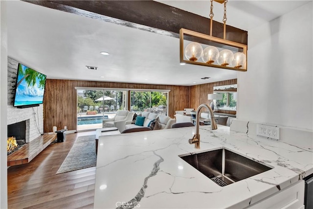 kitchen featuring light stone countertops, sink, hanging light fixtures, and a stone fireplace