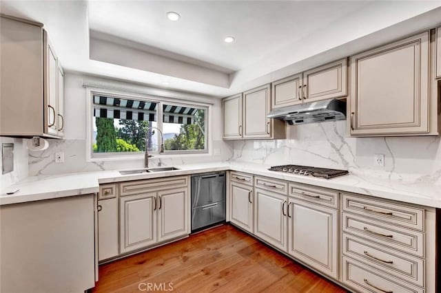 kitchen featuring stainless steel appliances, sink, backsplash, a raised ceiling, and light hardwood / wood-style flooring