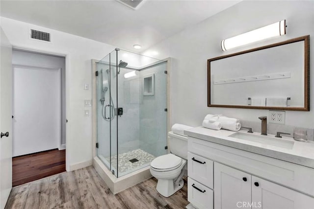 bathroom featuring toilet, vanity, wood-type flooring, and a shower with door