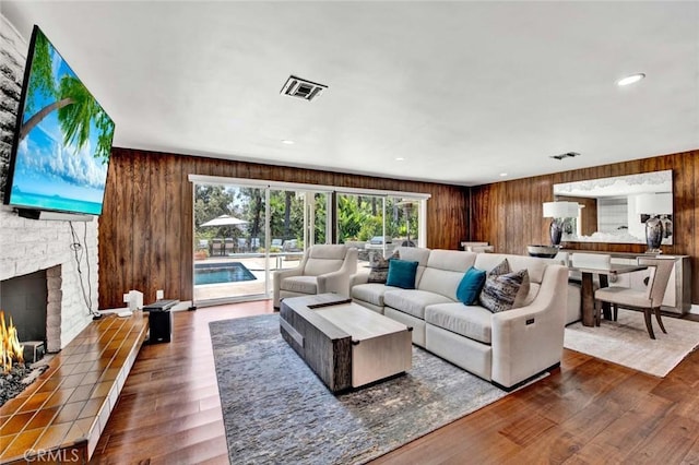 living room featuring dark hardwood / wood-style floors, wooden walls, and a stone fireplace