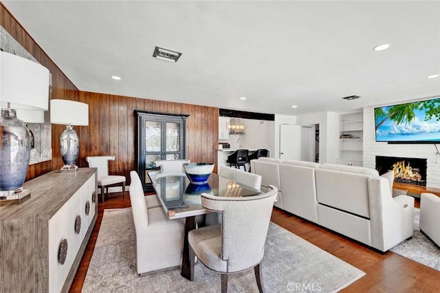 dining space with a brick fireplace, built in shelves, wood walls, and hardwood / wood-style floors