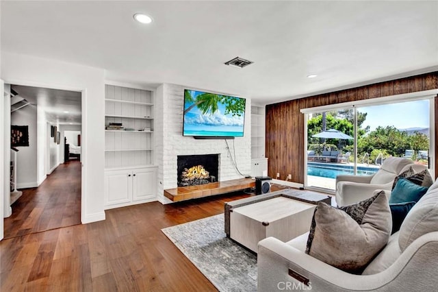 living room with a brick fireplace, dark wood-type flooring, and built in features