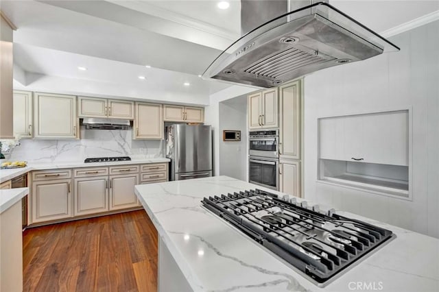 kitchen featuring island exhaust hood, crown molding, light stone countertops, appliances with stainless steel finishes, and cream cabinetry