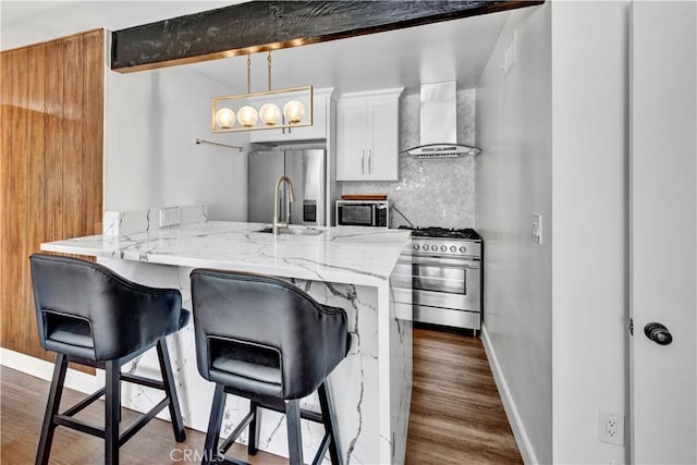 kitchen featuring appliances with stainless steel finishes, tasteful backsplash, decorative light fixtures, wall chimney range hood, and beam ceiling