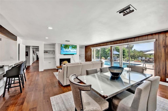 dining area featuring dark wood-type flooring, built in shelves, a fireplace, and wooden walls