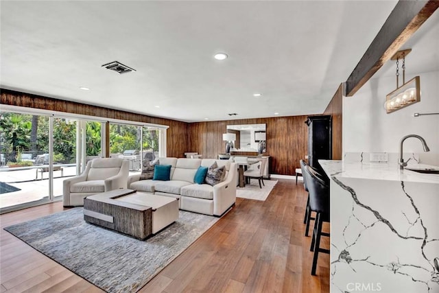 living room featuring wood walls, hardwood / wood-style floors, beamed ceiling, sink, and a chandelier