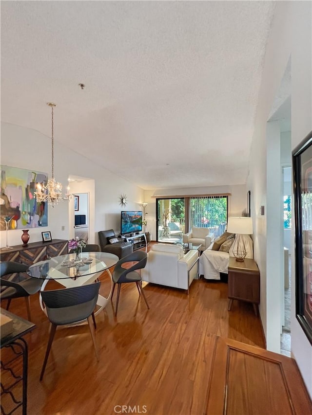 living room with lofted ceiling, a textured ceiling, wood-type flooring, and a chandelier