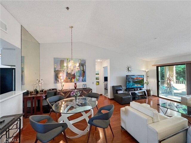 dining area with lofted ceiling, a notable chandelier, hardwood / wood-style flooring, and a textured ceiling