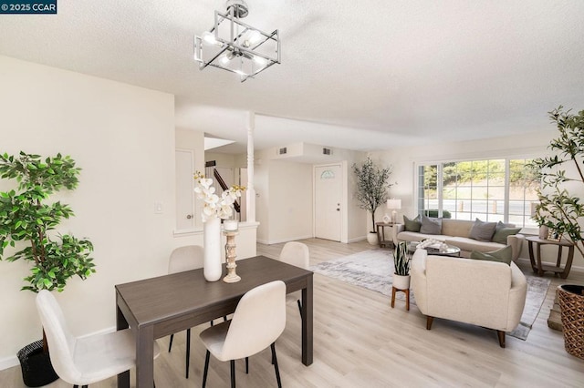 dining space featuring light hardwood / wood-style floors, a textured ceiling, and a notable chandelier