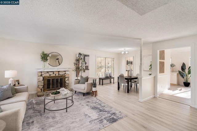 living room featuring a textured ceiling, light hardwood / wood-style flooring, and a stone fireplace