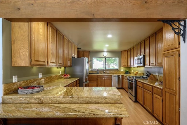 kitchen with appliances with stainless steel finishes, sink, kitchen peninsula, light stone counters, and light hardwood / wood-style flooring