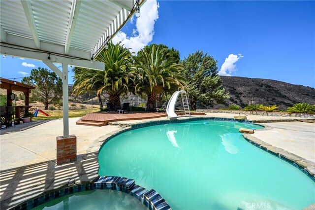 view of pool featuring an in ground hot tub, a patio area, a water slide, and a deck with mountain view