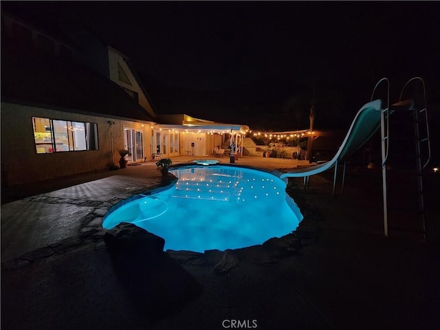 pool at twilight with a water slide and a patio