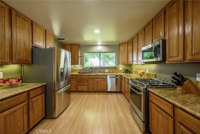 kitchen with light wood-type flooring, light stone countertops, stainless steel appliances, and sink