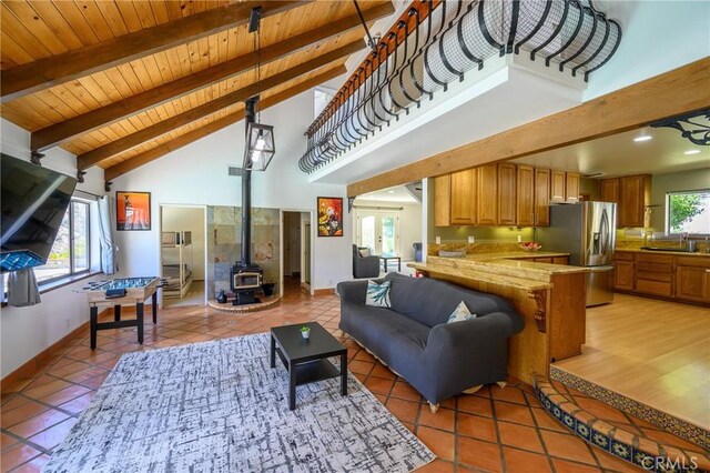 tiled living room featuring sink, beamed ceiling, a wood stove, high vaulted ceiling, and wooden ceiling