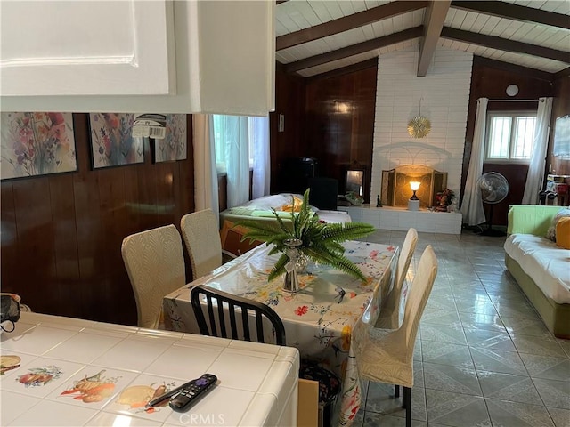 dining space with tile patterned flooring, lofted ceiling with beams, wooden walls, and wood ceiling