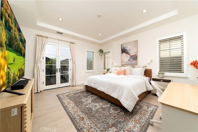 bedroom with multiple windows, a raised ceiling, access to outside, and french doors