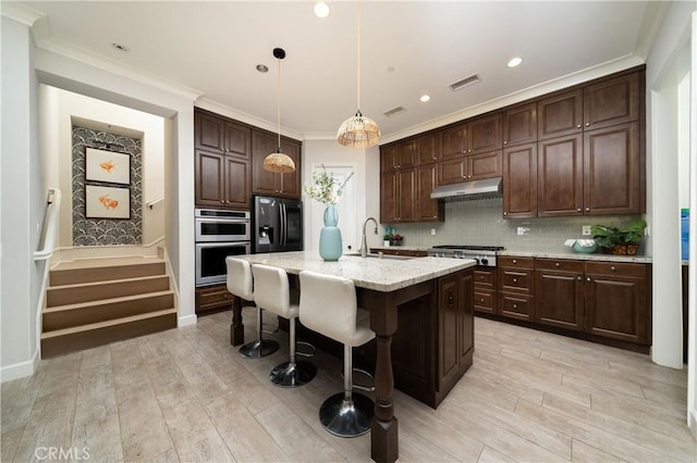 kitchen with stainless steel appliances, decorative backsplash, a kitchen island with sink, hanging light fixtures, and sink