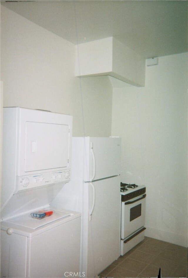 kitchen with tile patterned flooring, stacked washer and clothes dryer, white appliances, and white cabinetry