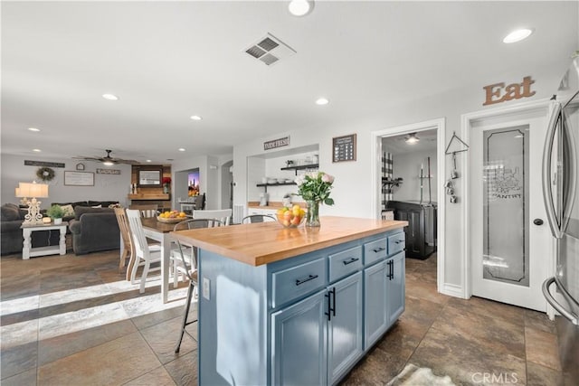 kitchen with ceiling fan, a kitchen island, a kitchen breakfast bar, blue cabinetry, and butcher block counters