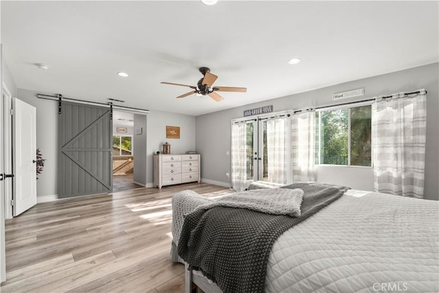 bedroom featuring ceiling fan, a barn door, and light wood-type flooring