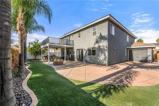 back of property featuring a lawn, a fire pit, a garage, a patio area, and a deck